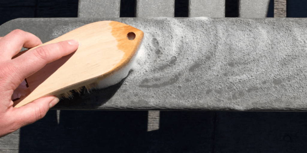 Using a brush to remove pink stains from patio furniture, restoring its clean and fresh appearance